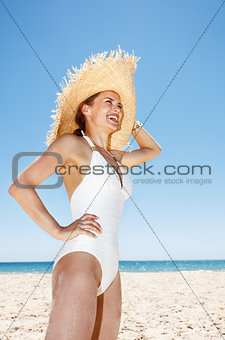 Smiling woman in straw hat at sandy beach looking into distance