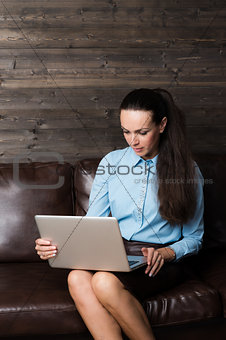 Happy brunette sitting on sofa in living room using laptop