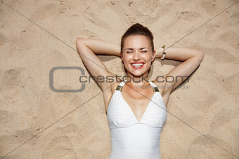 Portrait of smiling woman in swimsuit laying on the sand