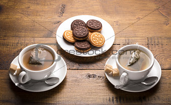 Set of two ceramic tea mugs with sachet and plates of cookies.