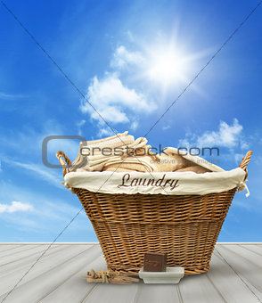 Laundry basket with clothes on rustic table against blue sky
