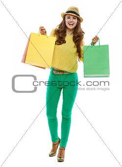 Smiling woman in hat and bright clothes showing shopping bags