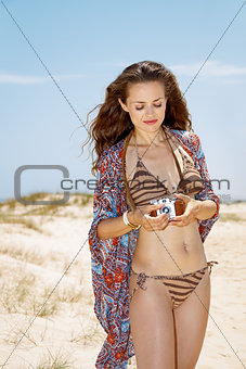 Bohemian young woman on white beach adjusting retro photo camera