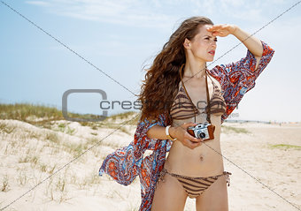 Bohemian woman with retro photo camera on beach looking aside
