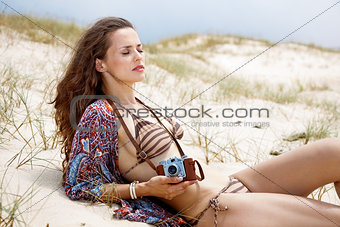 Relaxed bohemian woman with retro photo camera laying on beach