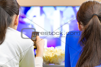 Two teenager girls laying down and watching tv