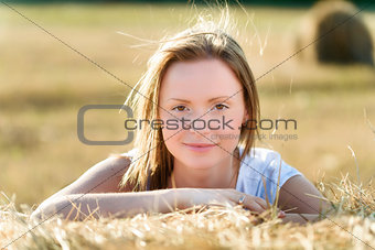 Portrait of a young woman who leans on a bale of hay