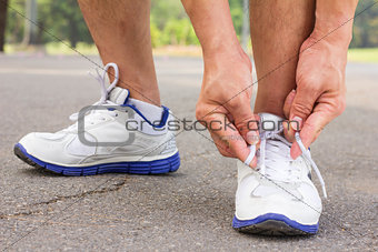 Men is tying shoes laces for jogging at park.