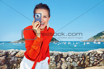 Happy woman taking photo with digital camera in front of lagoon