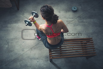 Upper view on fitness woman lifting dumbbell in urban loft gym