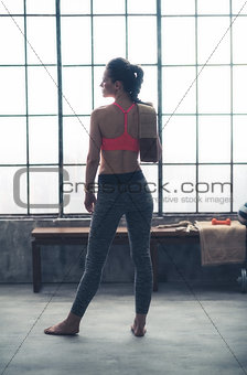Seen from behind fitness woman with towel standing in loft gym