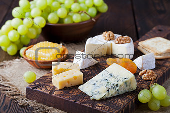 Assortment of cheese with honey, nuts and grape on a rustic cutting board