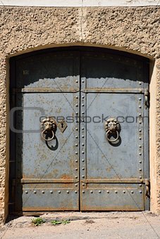 Old iron door with lion handles on a stone wall