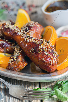Fried chicken drumsticks with sesame seeds and orange slices.