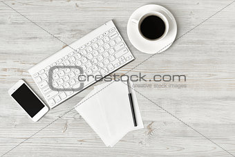 Workplace with cup of coffee, keyboard, smarthphone, white sheets and pen on wooden surface in top view.
