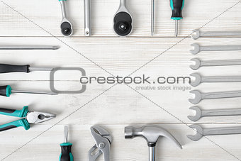 Top view of construction tools including hammer and different sized screwdrivers, wrenches on wooden surface with open space.