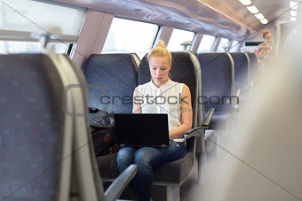 Woman travelling by train working on laptop.