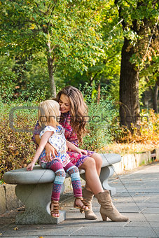 Happy mother and daughter sitting on the bench at the park.