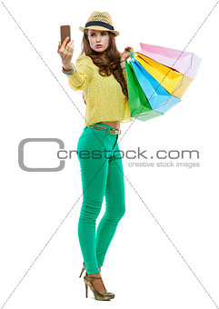 Woman in hat with shopping bags taking selfie with smartphone