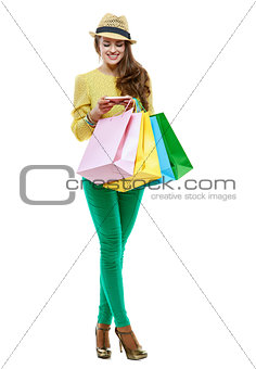 Smiling woman with shopping bags writing sms on white background