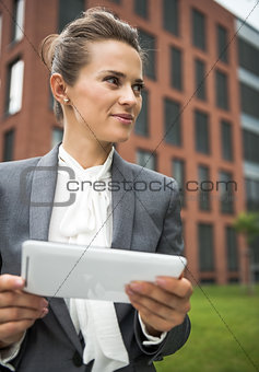 Business woman with tablet PC near office building looking aside