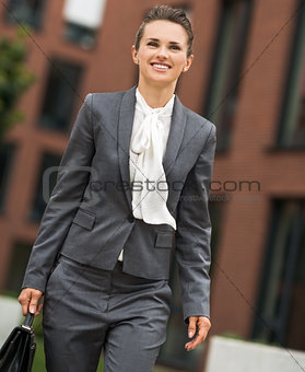 Happy business woman with briefcase walking at office district