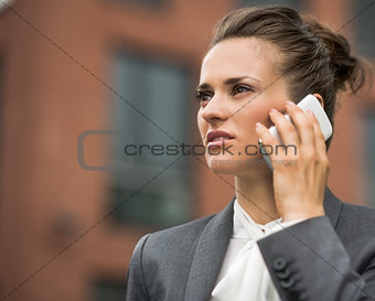 Modern business woman against office building talking smartphone