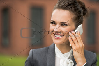 Smiling business woman near office building talking smartphone