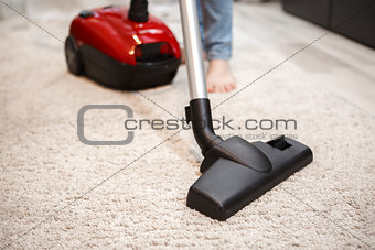 Maid cleaning carpet with modern red vacuum cleaner
