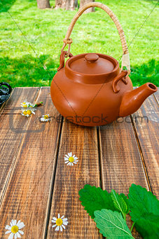 Brown teapoton on wooden with mint and chamomile table in garden and on nature background. Tea concept. Closeup.