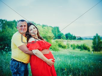 Pregnant woman and her husband with hands on belly outdoors