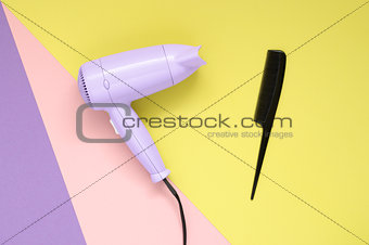 Hair dryer and comb on colorful paper background