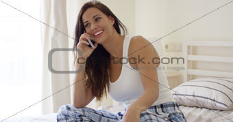 Young woman sitting on a bed chatting   mobile