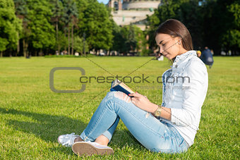 Girl-student sit on lawn and reads textbook.