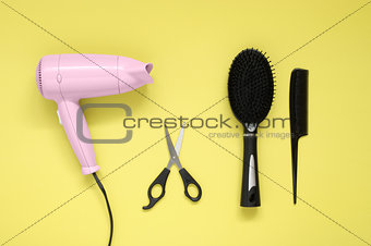 Hair dryer, brush, comb and scissors on yellow paper background