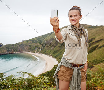 woman hiker taking selfie with smartphone in front of ocean