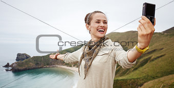 woman hiker taking selfie in front of ocean view landscape