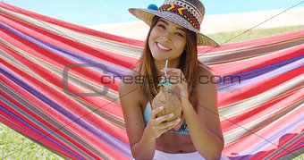 Woman with coconut drink and sitting in hammock