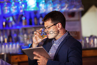 Businessman with tablet drinking whisky in bar