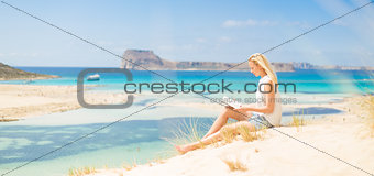 Woman reading book, enjoying sun on beach.