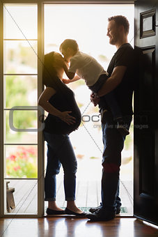 Young Son Kissing Pregnant Mom with Daddy in Doorway