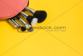 Make up brushes in a pink cosmetic bag on bright yellow backgrou