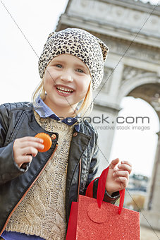 smiling child near Arc de Triomphe holding French macaroon