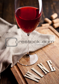 Glass of red wine on wooden board with letters and corks