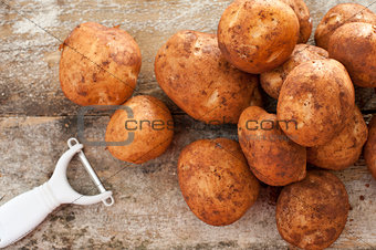 Pile of round baking potatoes beside peeler