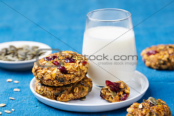 Pumpkin, oat cookies with cranberries, maple glaze and glass of milk on a blue textile background.