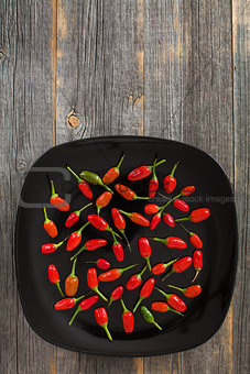 Red and green hot peppers on a black plate  old wooden boards