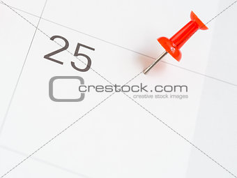 Red pin pinned on the 25th date of the month on calendar paper