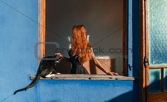Beautiful girl with red hair and cat at the window