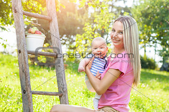 Mother with baby picking apples from an apple tree